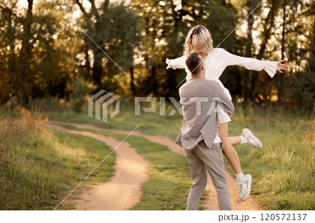 Young happy couple walking in the park. A man circles a woman in his arms. 120572137