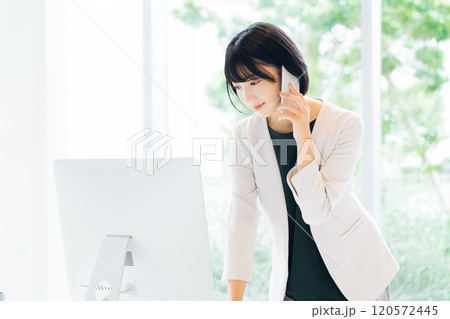 パソコンを見ながら電話をする女性 パソコンを見ながら電話をする女性 120572445