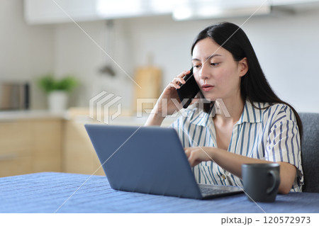Asian woman talking on phone checking laptop solving problem 120572973