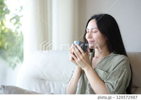 Satisfied asian woman enjoying smelling coffee at home 120572987