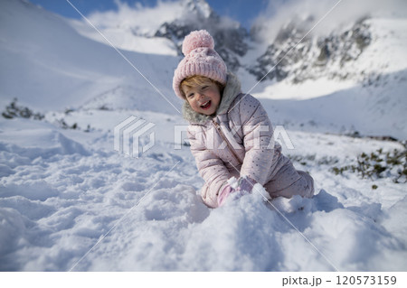 Portrait of small girl enjoying winter holiday in the mountains with family, playing in snow. 120573159