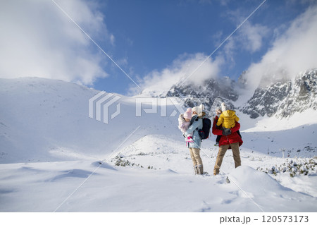 Young family is enjoying winter holiday in the mountains, standing in the middle of snowy landscape. 120573173