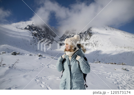 Woman standing in the middle of the snowy nature looking at the winter landscape around her, smiling. 120573174