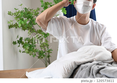 ベッドで頭痛に苦しむマスク姿の若い男性 120573811