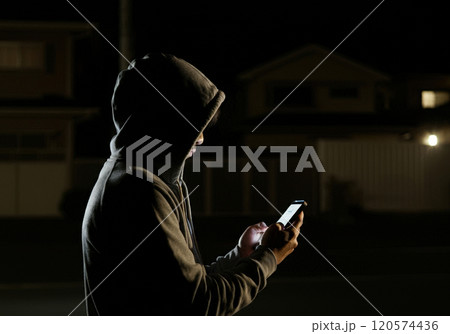 夜の住宅街で闇バイトの時間を待つ男 120574436