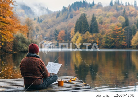 Person sketching by a lake with a view of fall foliage. Person sketching by a lake with a view of fall foliage. 120574579