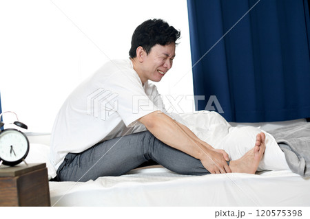 ベッドの上で足の痛みに悩むアジア人男性 120575398