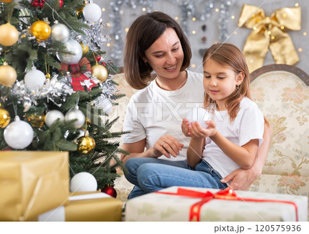 Mom and daughter holding Christmas decorations on Christmas tree 120575936