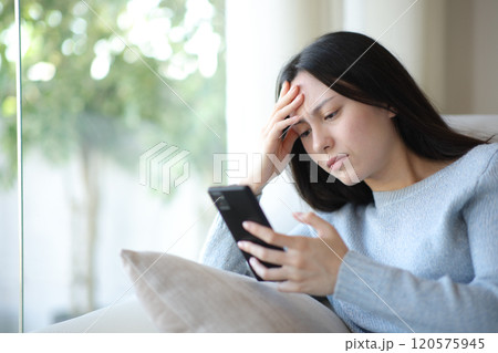 Worried asian woman checking cell phone at home 120575945