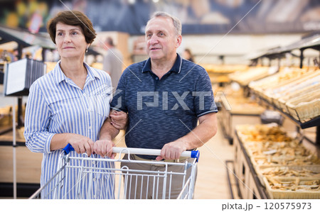 Mature family of retirees examines bread and pastries in grocery section of a supermarket 120575973