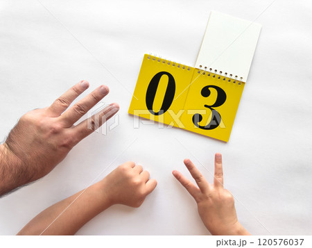 Counting hands with yellow calendar displaying number three for learning 120576037