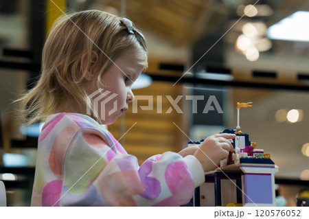 Kids Play Room. Cute girl child plays with colored plastic parts of the constructor, creates buildings, equipment, transport, the concept of the development of creativity, fine motor skills. 120576052