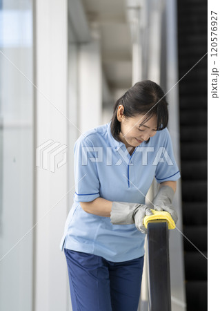 エスカレーターの手すりを拭くミドルの女性清掃スタッフ 120576927