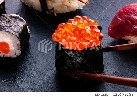 Sushi rolls on a black background. Ikura maki roll with chopsticks 120578288