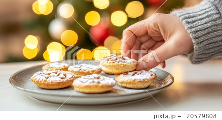 Cozy hands place freshly baked mince pies on a beautiful plate for festive holiday celebrations in a decorated kitchen Cozy hands place freshly baked mince pies on a beautiful plate for festive holiday celebrations in a decorated kitchen 120579808