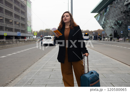 Smiling 30s lady tourist woman in casual clothing with smart phone taking taxi from an airport. Luggage on the city street. Travel concept. 120580065