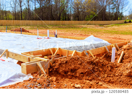 Preparing foundation at construction site with wooden forms filled with gravel surrounded by covered area with protective plastic to prevent moisture Preparing foundation at construction site with wooden forms filled with gravel surrounded by covered area with protective plastic to prevent moisture 120580485