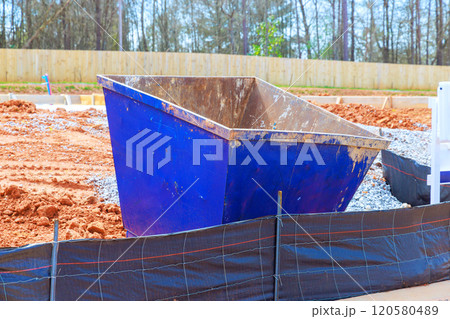 Dumpster sits on construction site surrounded by dirt gravel area is partially cleared 120580489