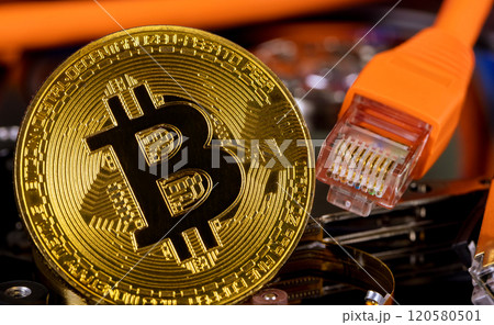 Gold colored Bitcoin coin rests top hard drive, with Ethernet cables visible in background. Gold colored Bitcoin coin rests top hard drive, with Ethernet cables visible in background. 120580501