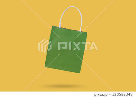 Green paper shopping bag isolated on yellow background 120582349
