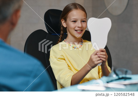 Smiling Girl Holding Mirror While Sitting in Dental Chair Smiling Girl Holding Mirror While Sitting in Dental Chair 120582548