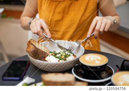 Woman eating tasty Shakshuka at cafe. Middle eastern traditional dish. Fried eggs with tomatoes and cup of coffee. Concept of easy breakfast. Food banner Woman eating tasty Shakshuka at cafe. Middle eastern traditional dish. Fried eggs with tomatoes and cup of coffee. Concept of easy breakfast. Food banner 120584756