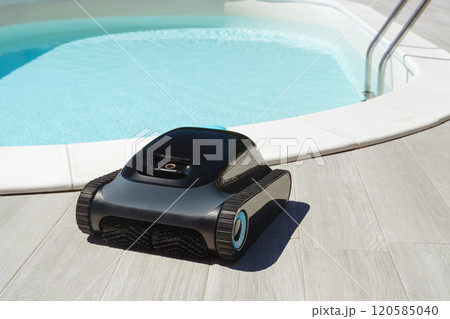 robotic pool cleaner in front of swimming pool with clear blue water 120585040