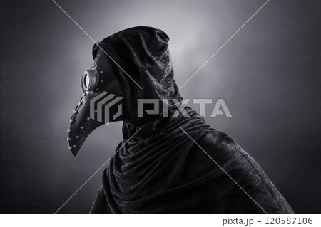 Plague doctor in hooded cloak at night over dark misty background 120587106