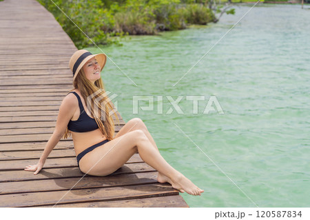 Woman in swimsuit sitting on a pier at Lake Bacalar. Quintana Roo, Mexico travel, summer relaxation, and waterfront serenity concept Woman in swimsuit sitting on a pier at Lake Bacalar. Quintana Roo, Mexico travel, summer relaxation, and waterfront serenity concept 120587834