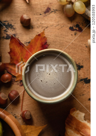 Cozy autumn breakfast close up with coffee, croissants, autumn fruits, grapes, pears and hazelnuts on wooden table. Top view 120588993