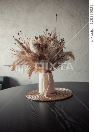 Stylish modern dried flower arrangement in a cream vase at home room. Composition with many different dried flowers in vases, on a light background. 120589023