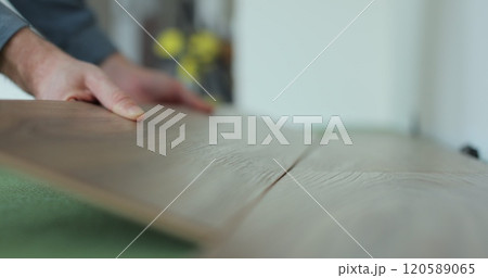 Man kneeling and installing wood laminate floor in a home. Closeup on male hands. 120589065