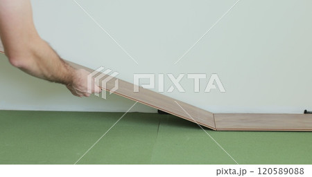 Man kneeling and installing wood laminate floor in a home. Closeup on male hands. Man kneeling and installing wood laminate floor in a home. Closeup on male hands. 120589088
