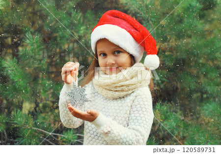 Christmas portrait of happy smiling little girl child in santa red hat with snowflake toy outdoors 120589731
