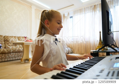 Young girl enjoying music while playing keyboard in a bright living room 120589909