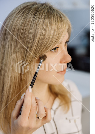 Close up of a woman applying highlighter with a brush for a natural and radiant makeup look Close up of a woman applying highlighter with a brush for a natural and radiant makeup look 120590620