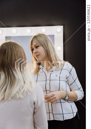 Professional makeup artist consulting a client in a studio setting with illuminated mirrors 120590621