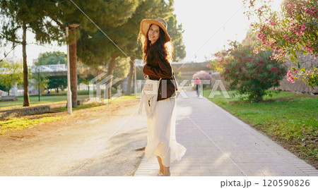 A carefree woman wearing a stylish hat walks joyfully through a vibrant, scenic park 120590826