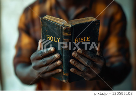 African American man holds an open black holy Bible in his hands. 120595108