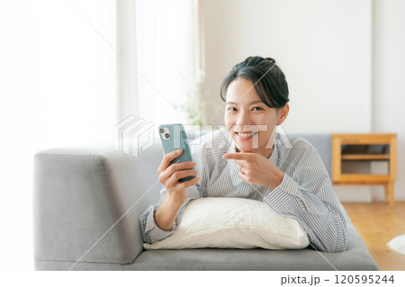 ソファで寝転んでスマホを見る女性 120595244