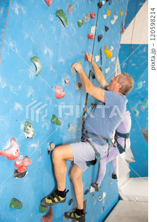 Adult man climbing wall with safety rope 120598214