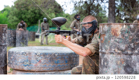 Paintball player in camouflage and mask aiming with gun in shootout Paintball player in camouflage and mask aiming with gun in shootout 120598228