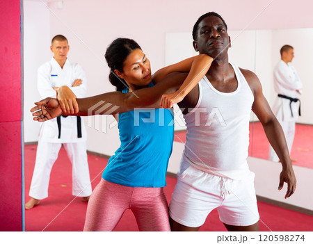 Woman exercising self-defence moves, trainer watching them 120598274