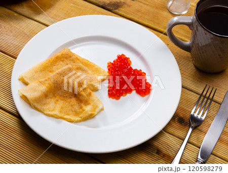 Ruddy pancakes with pile spoonful sturgeon roe. Dish is complemented by cup of tea 120598279