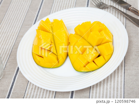 Two halves of ripe yellow mango cut into cubes lie on white round plate Two halves of ripe yellow mango cut into cubes lie on white round plate 120598746