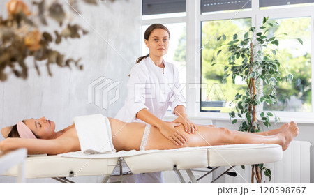Female masseur performs patting during spa procedure of front zone thigh for girl 120598767