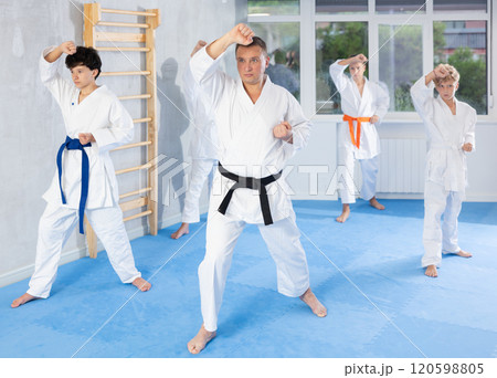 Middle-aged trainer practicing kata standing in row with preteen attendees of karate classes 120598805