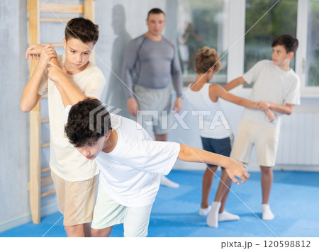 Diligent preteen student twisting his opponent's arm in sports hall 120598812