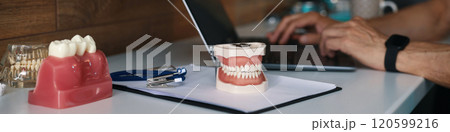 Typing on Laptop near Dental Prostheses and Tools 120599216