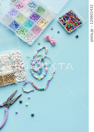 Crafting colorful beaded jewelry on a blue surface with tools and a variety of beads 120601432